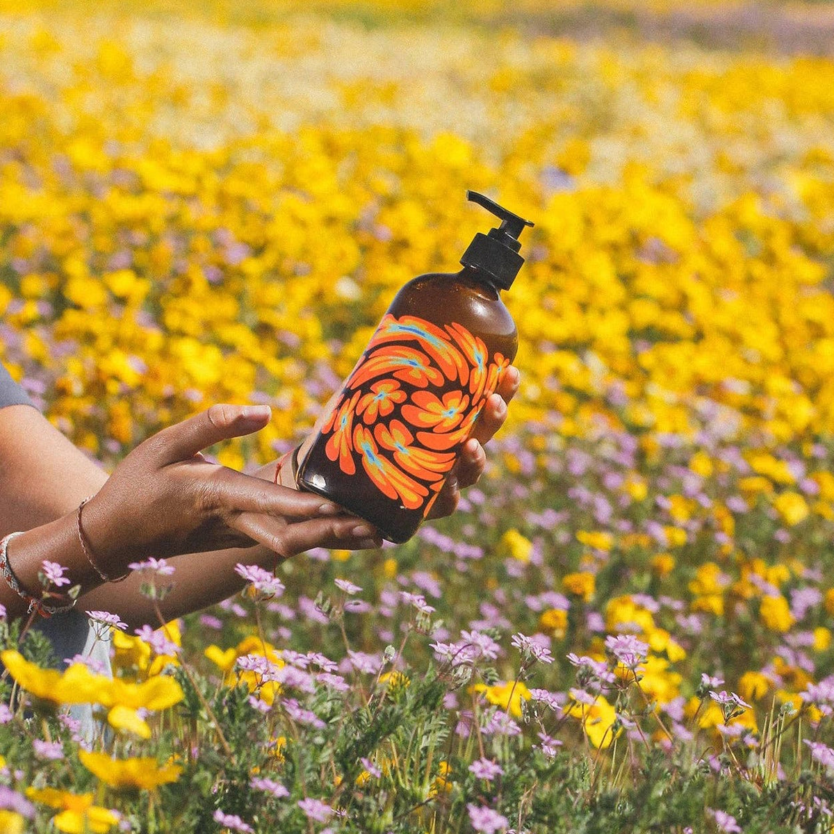 person holding floral bottle in a field of flowers