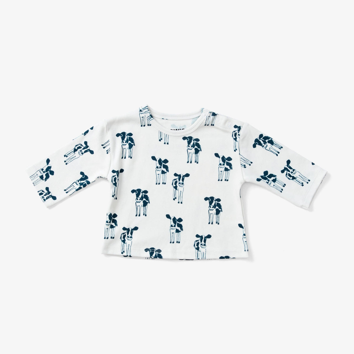 A white long-sleeve baby top with an all-over navy blue cow print, laid flat against a light gray background.