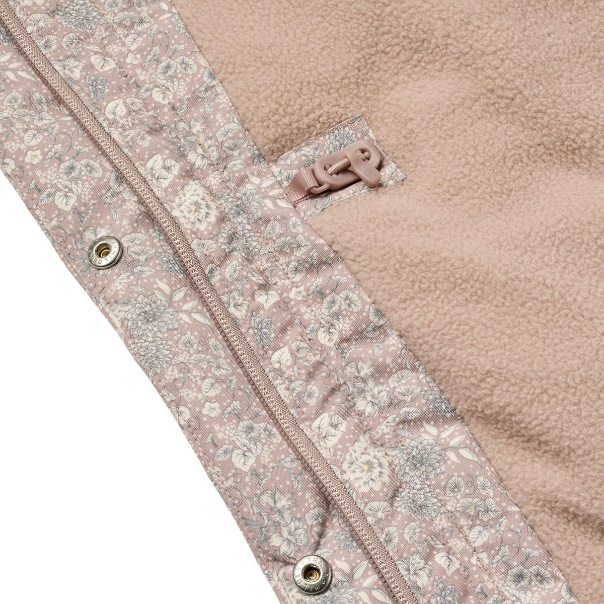 Close-up of a fleece jacket showing a soft blush pink fleece lining and a matching floral-patterned outer fabric with a zipper and snap buttons.