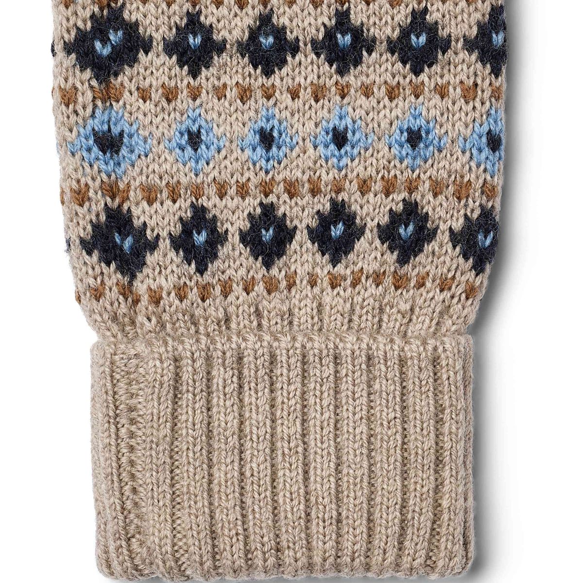 Close-up of a knitted sleeve or cuff in a warm beige/tan wool, featuring a Fair Isle pattern with navy, light blue, and brown motifs, and a ribbed knit cuff at the bottom.