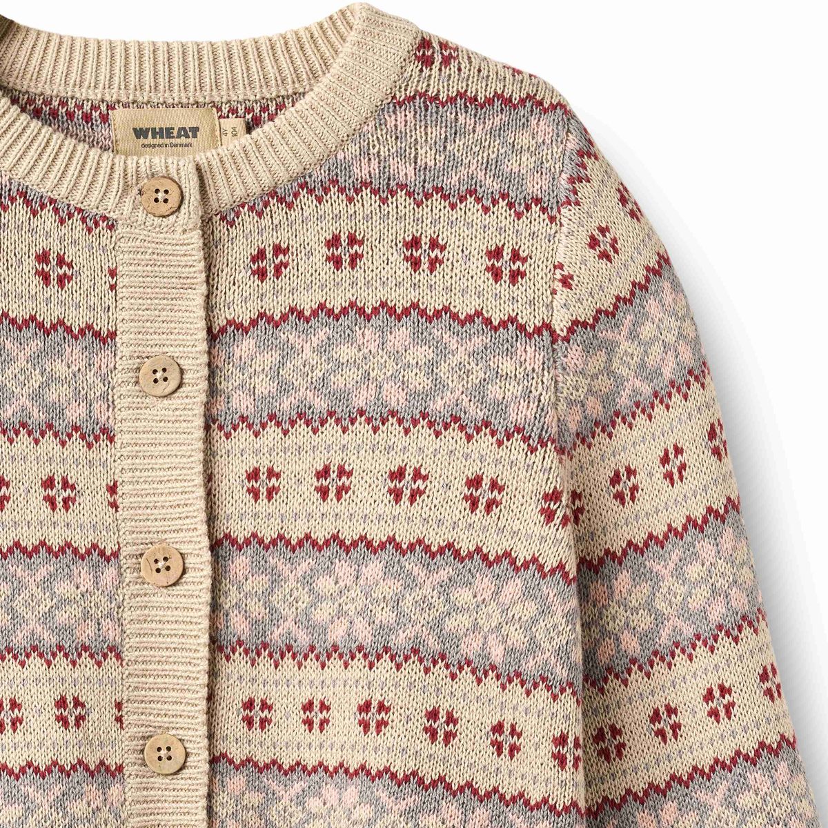 Close-up of a knit cardigan sweater with a cream base, red and gray Fair Isle style horizontal patterns, and a button-front closure. A woven neck label reads WHEAT.