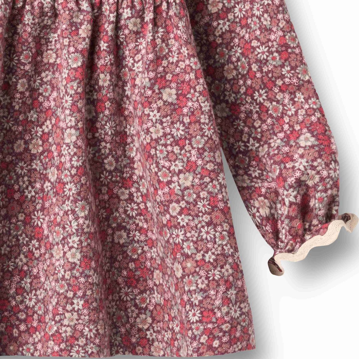 Close-up of a long-sleeve dress with an all-over small floral print in dusty pink, red, cream, and muted brown on a white background.