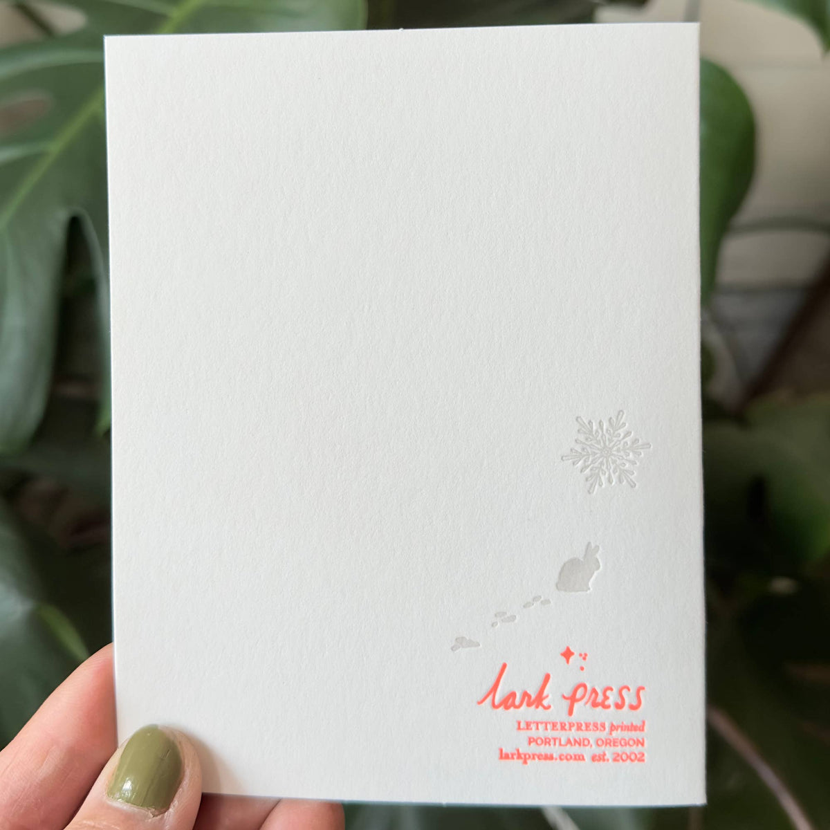 White card with 'lark press' text held by a hand against a green leafy background