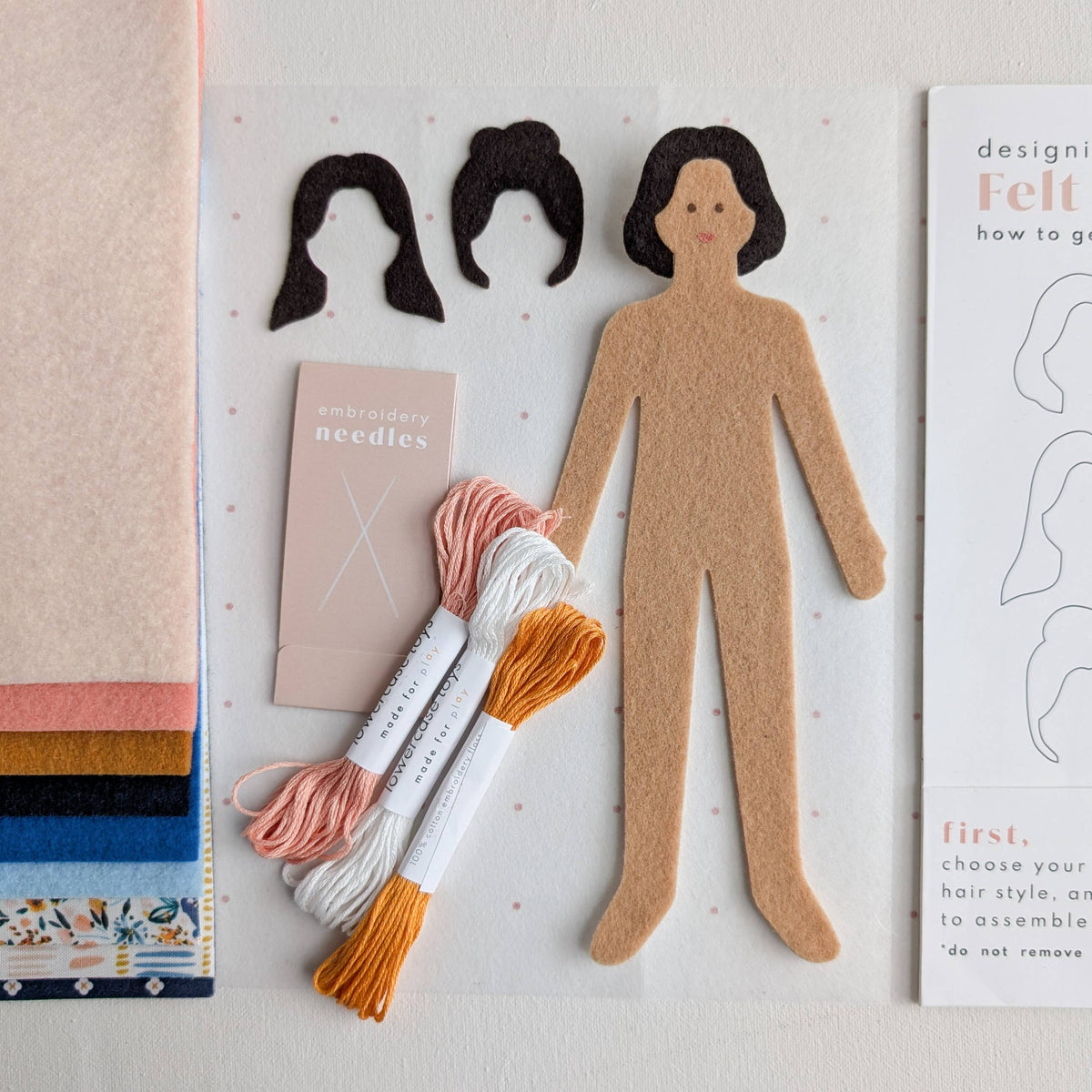 Felt craft kit with customizable paper dolls, embroidery needles, and thread on a light background.