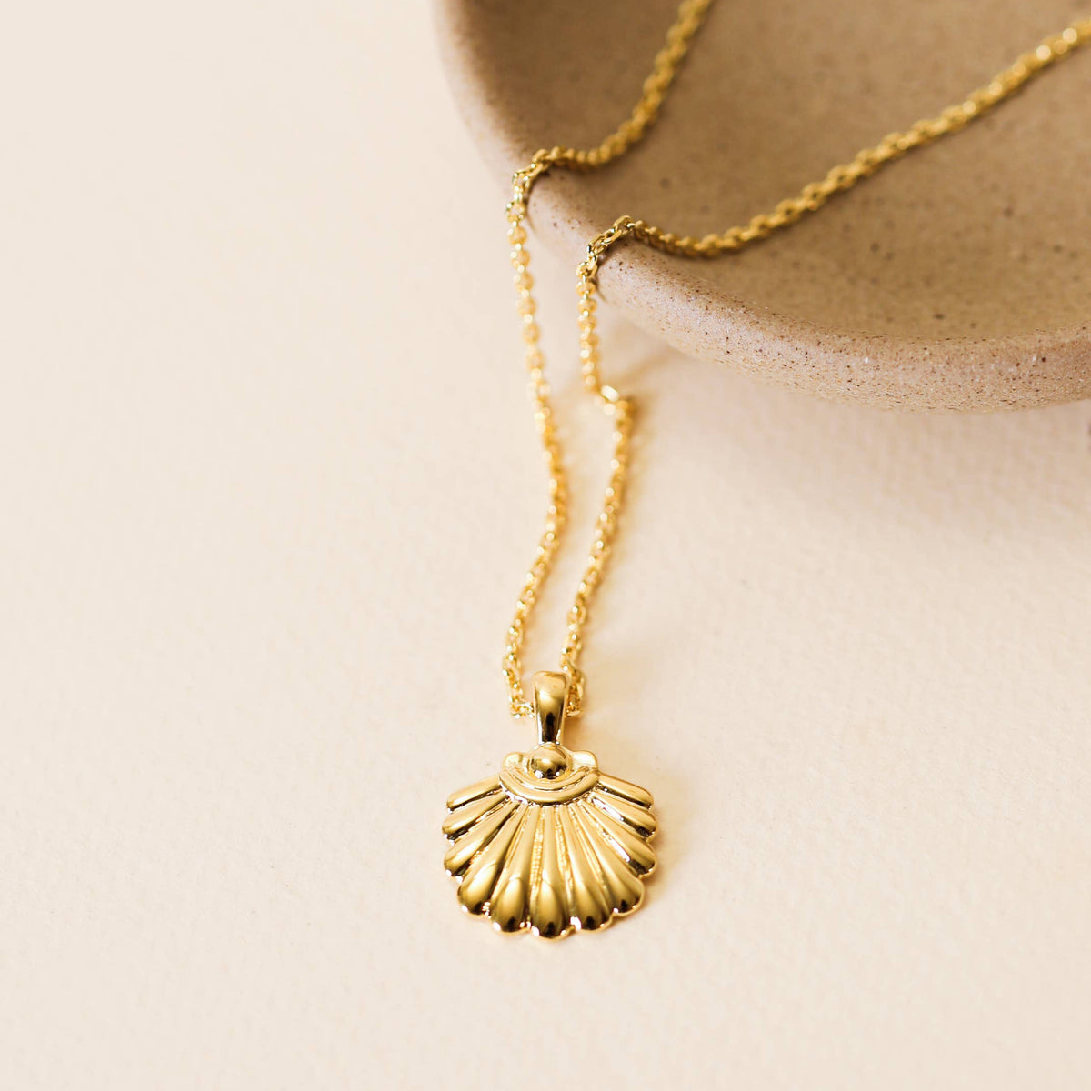 Gold necklace with a shell pendant on a beige background
