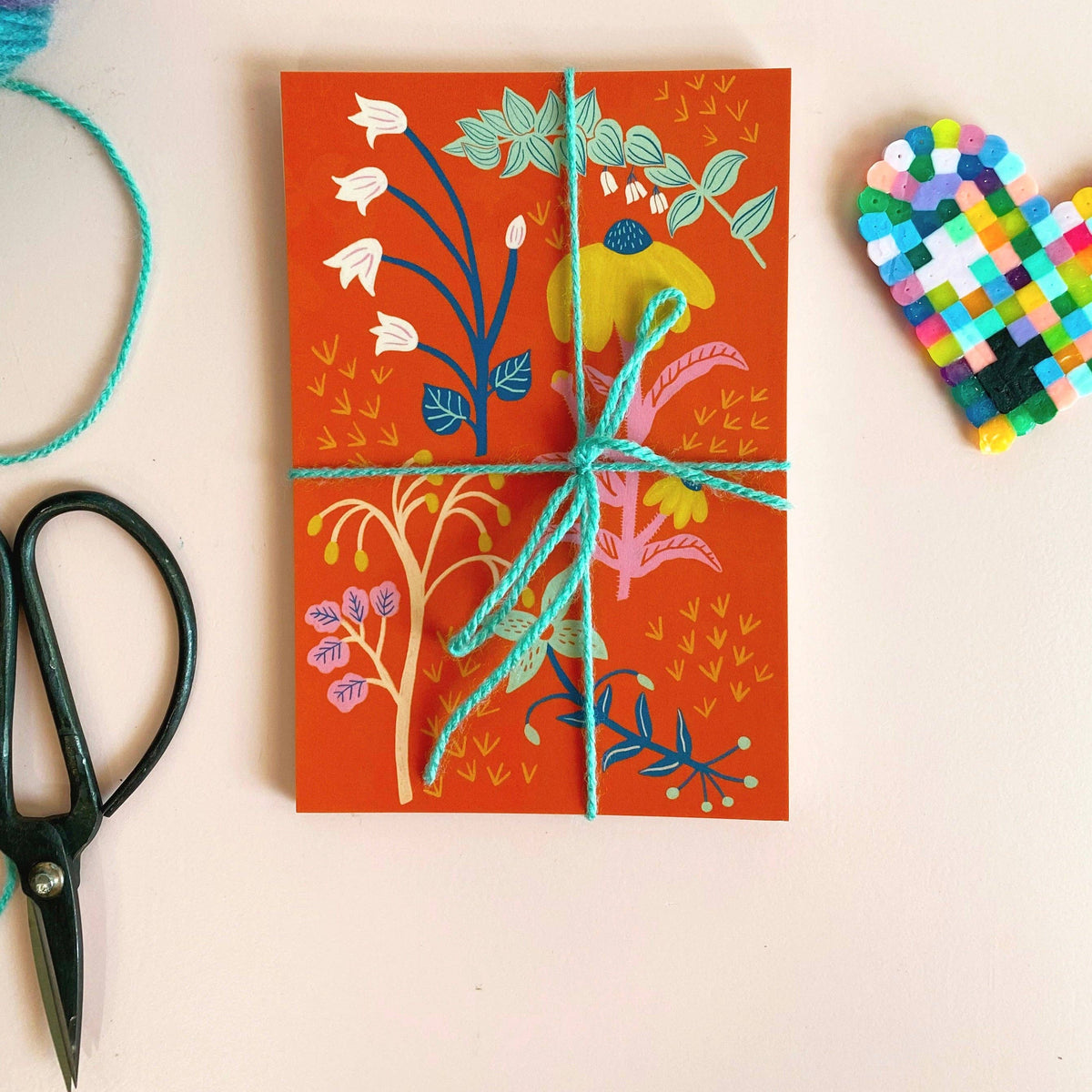 Decorative package with floral design on an orange background, surrounded by crafting tools.