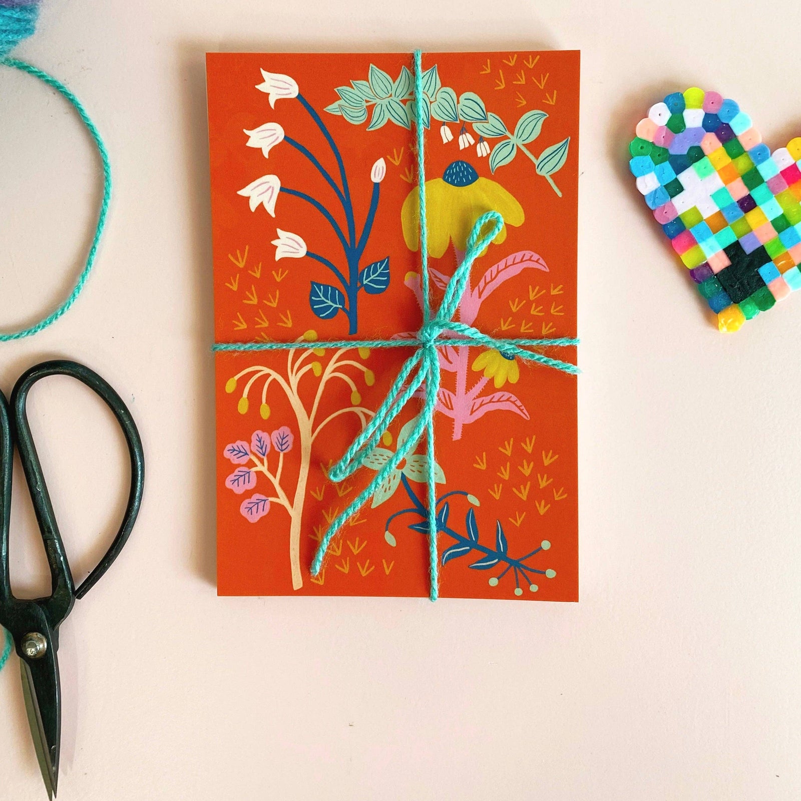 Five colorful floral greeting cards on a white surface with yarn and wooden swan decorations.