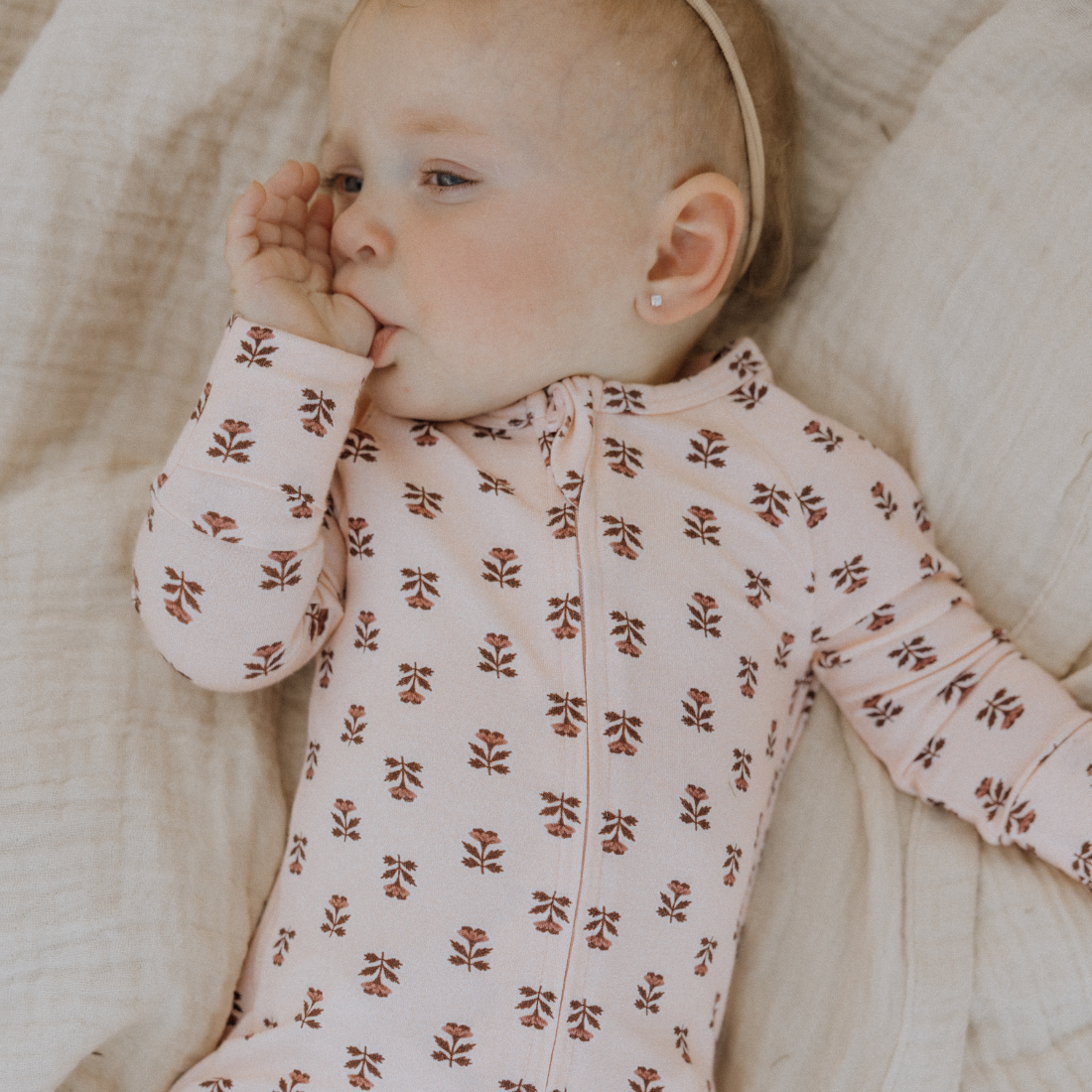 Baby wearing a pink floral onesie lying on a soft surface