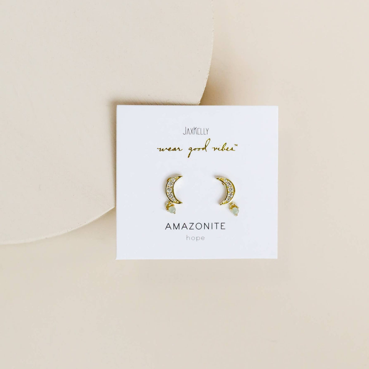 Pair of gold moon stud earrings on a white card with text on a beige background