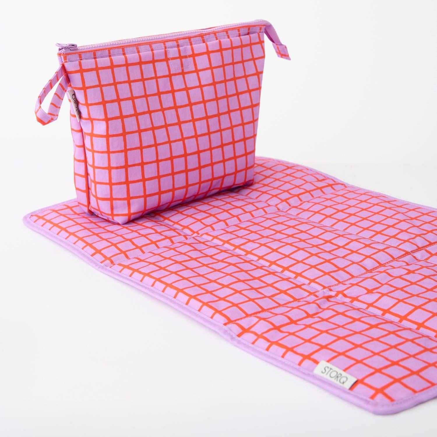 A pink and orange grid-patterned zippered pouch with a matching wrist strap, photographed on a clean white background.