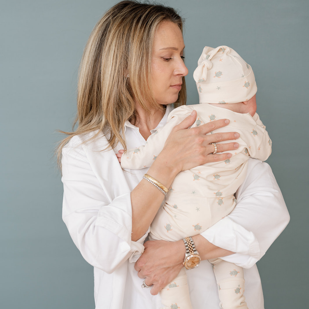 Woman holding a baby dressed in white against a gray background