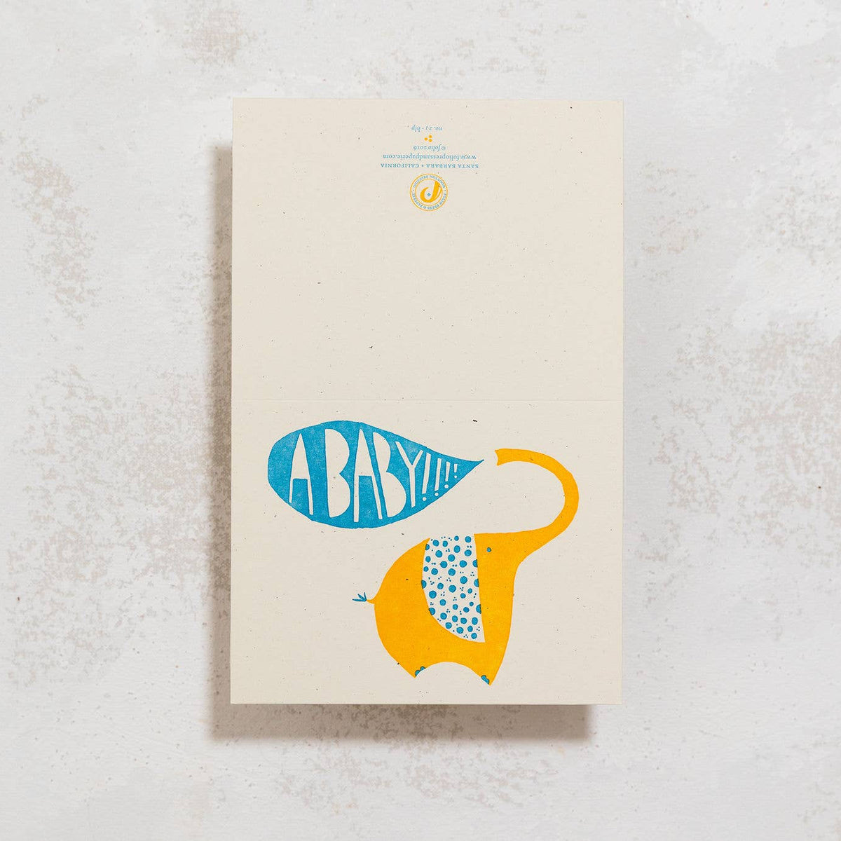 A vertical art print titled 'ABABY' featuring a stylized yellow elephant and blue patterned elements on a cream background, displayed on a textured light gray surface.