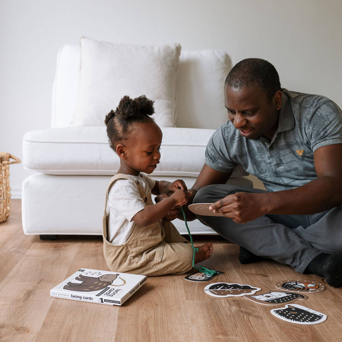 Man and child playing with cards on a wooden floor in a living room.