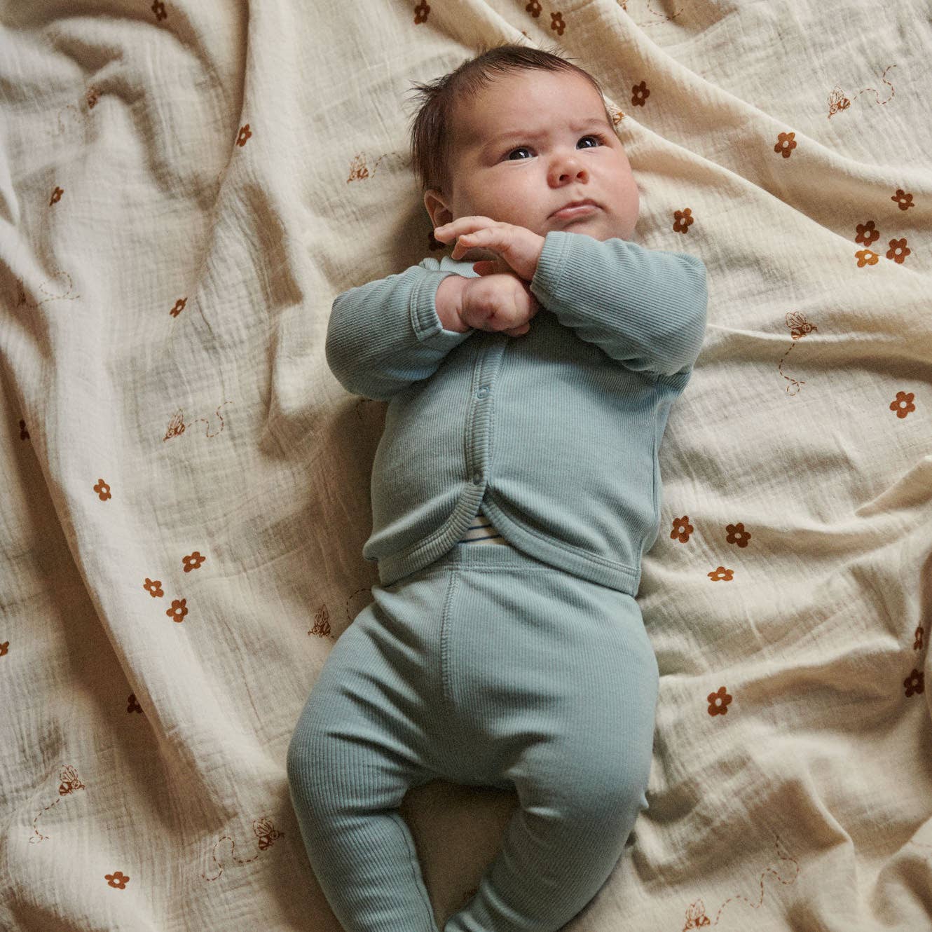 Baby in a light blue outfit lying on a soft, patterned blanket