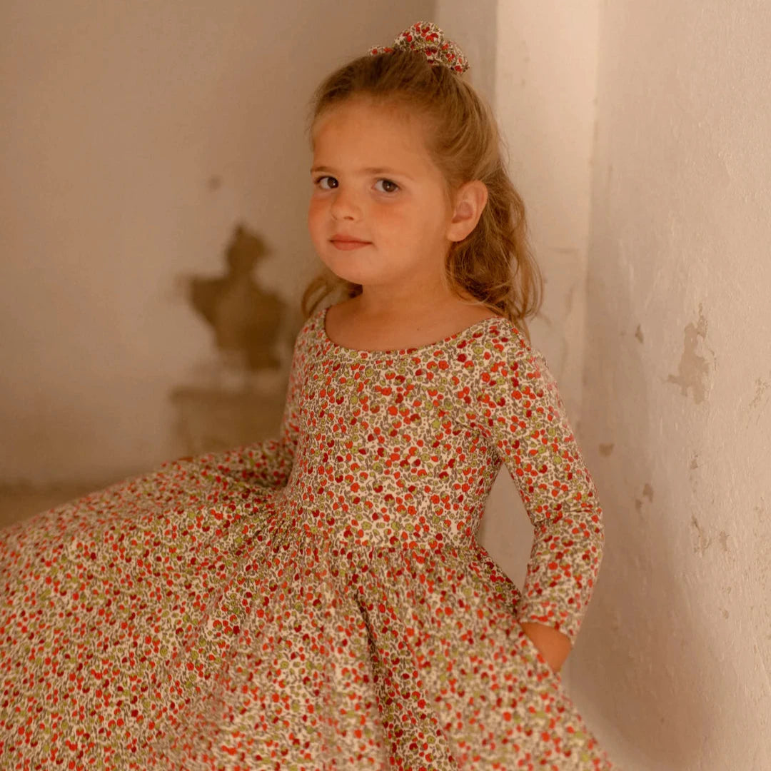 Young girl in a floral dress standing against a textured wall.
