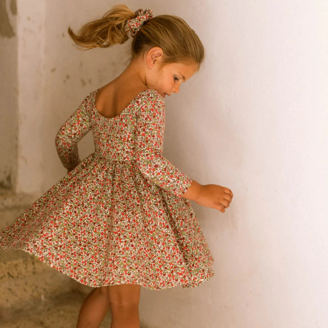 Young girl in a floral dress standing against a textured wall.