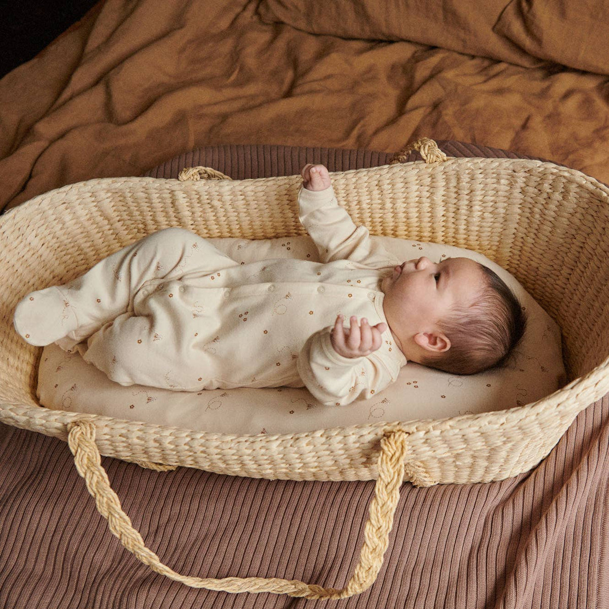 Newborn baby in a woven crib with brown bedding