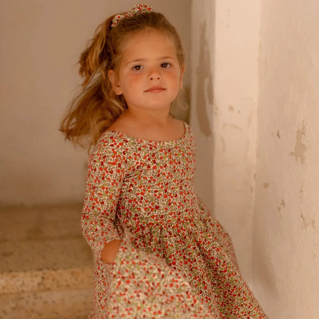 Young girl in a floral dress standing against a neutral wall.