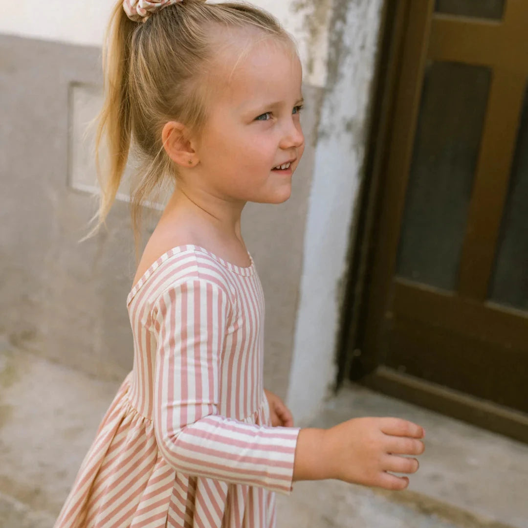 Young girl in a striped dress standing outdoors near a door.