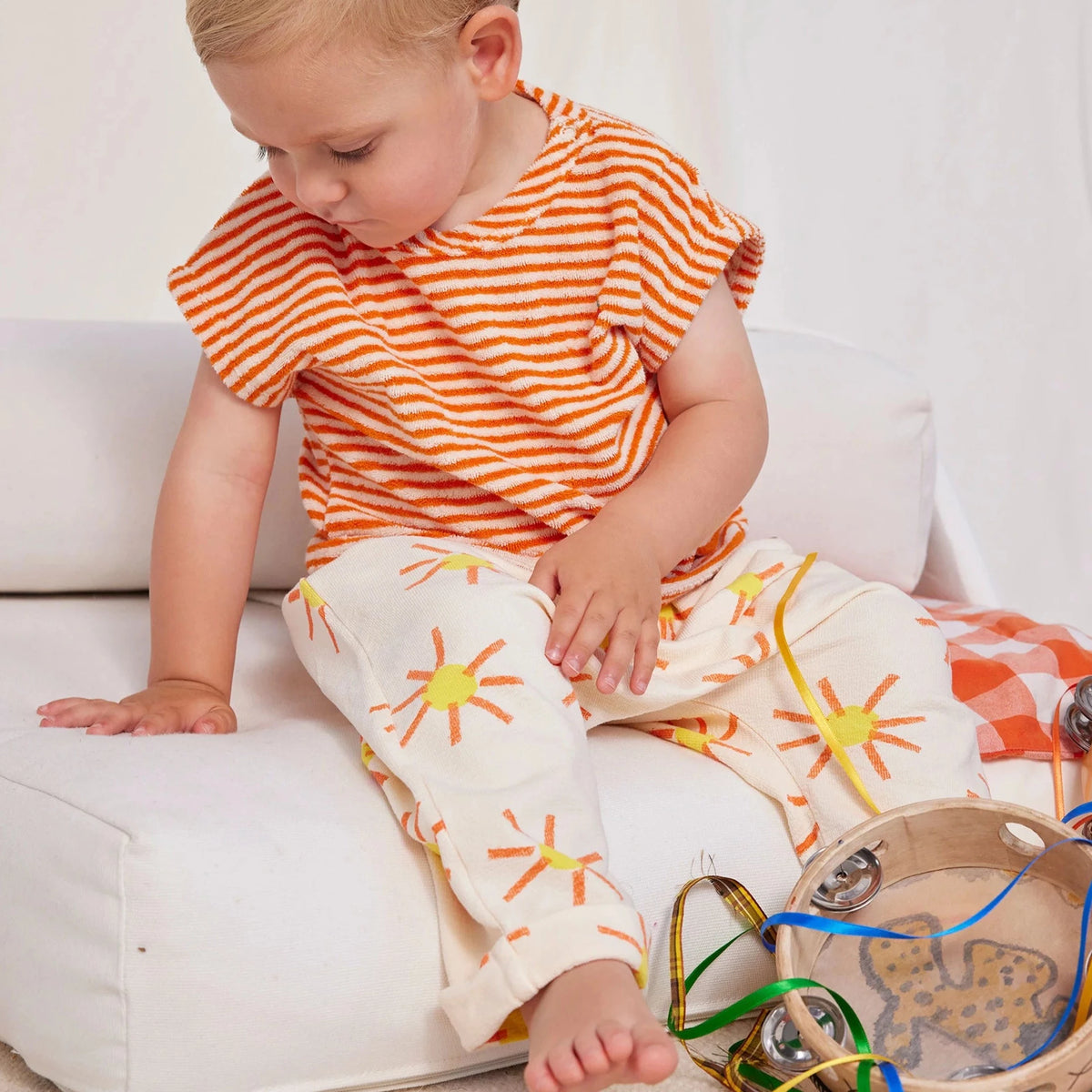 child wearing sun print pants with orange striped shirt