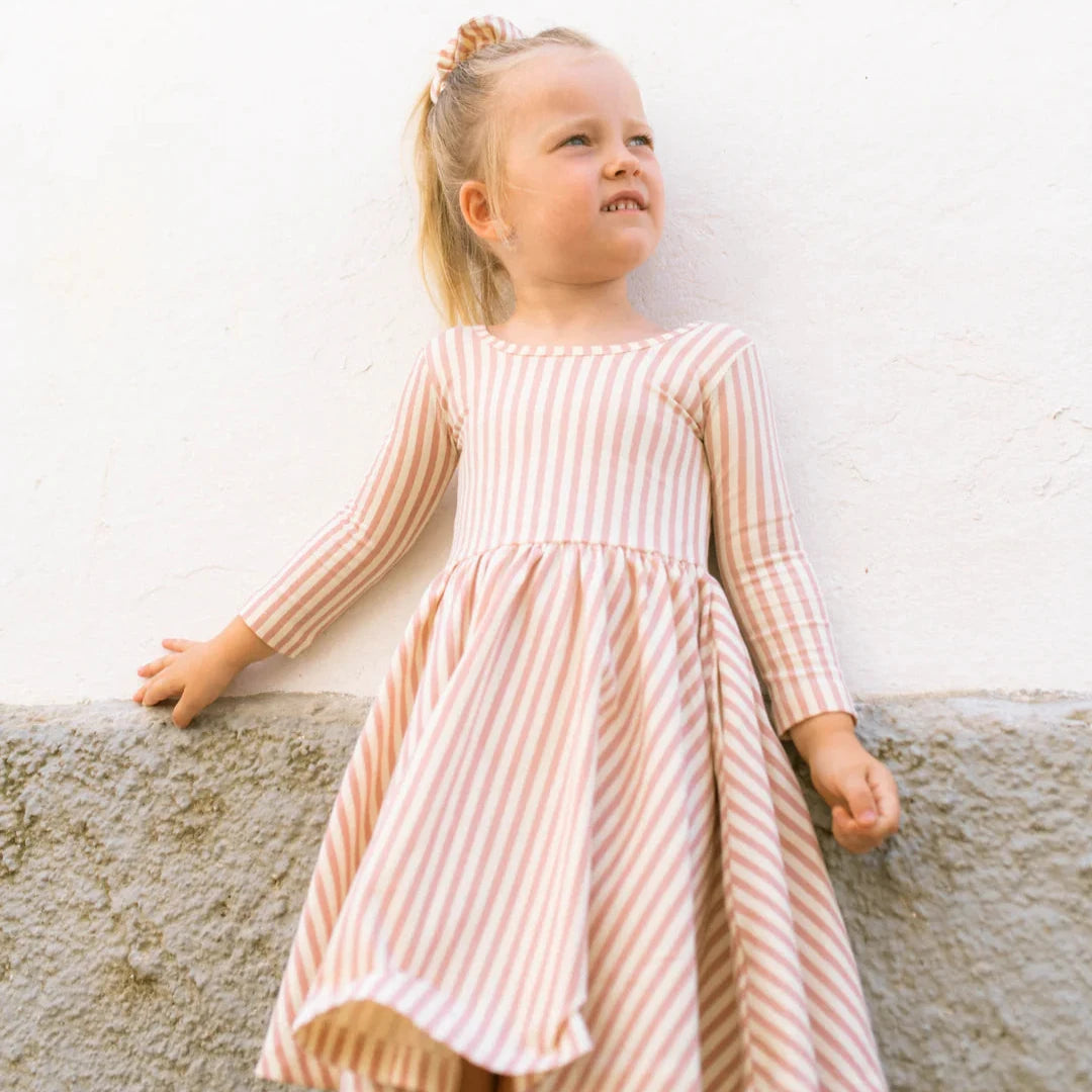 Young girl in a striped dress standing outdoors near a door.