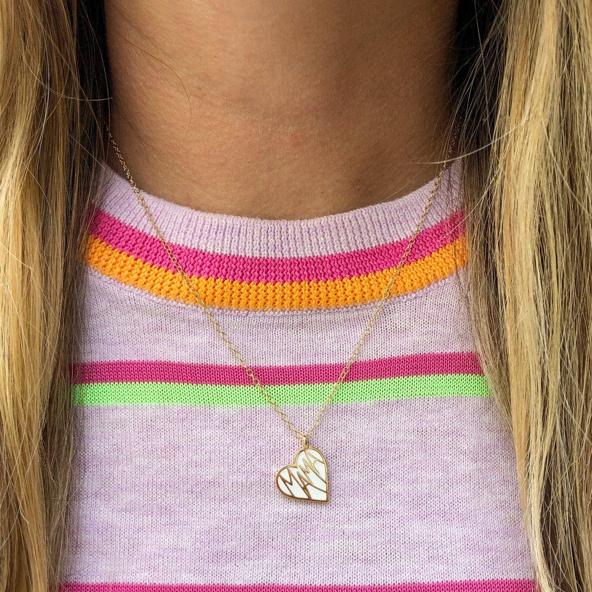 Gold necklace with a heart-shaped pendant in a clear packaging tube on a pink background