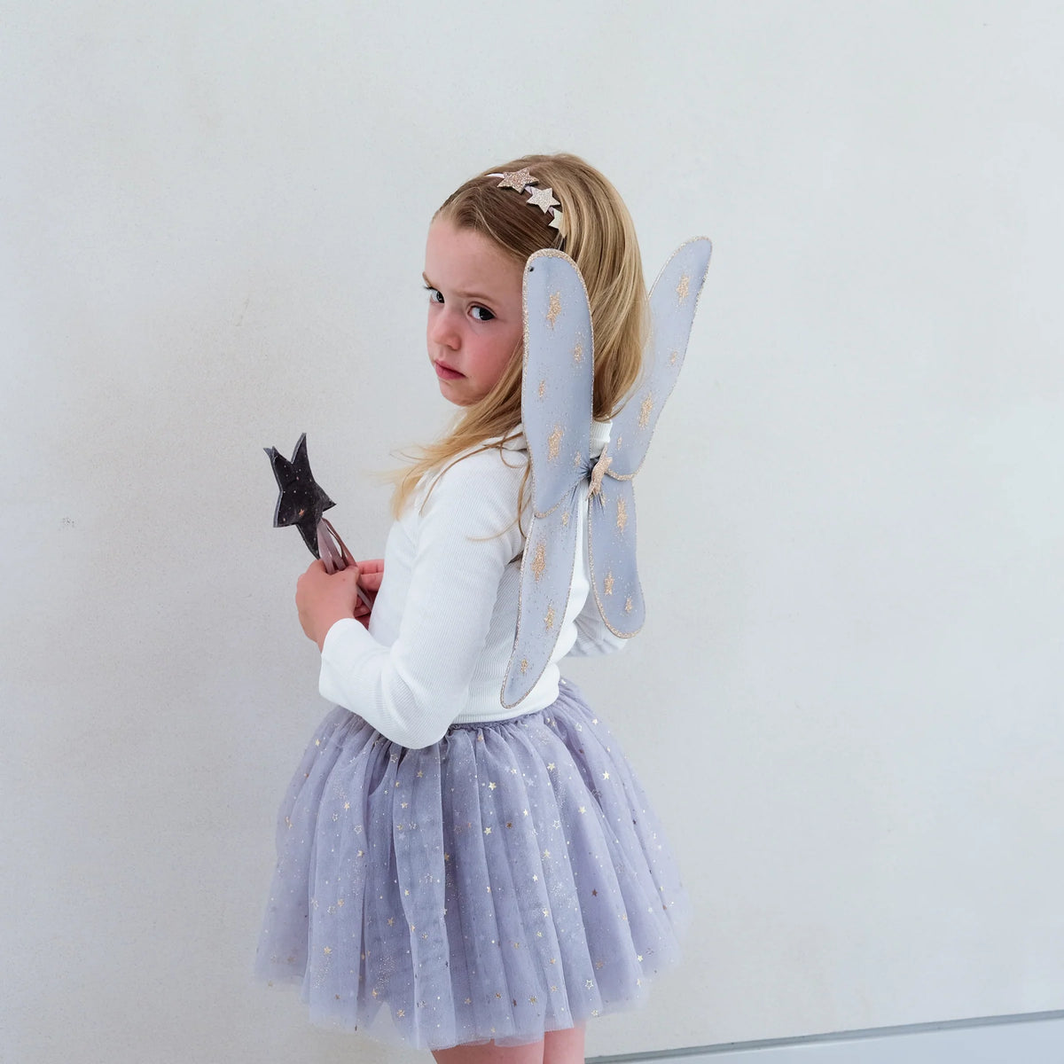 Child wearing a costume with butterfly wings and a star wand against a plain background