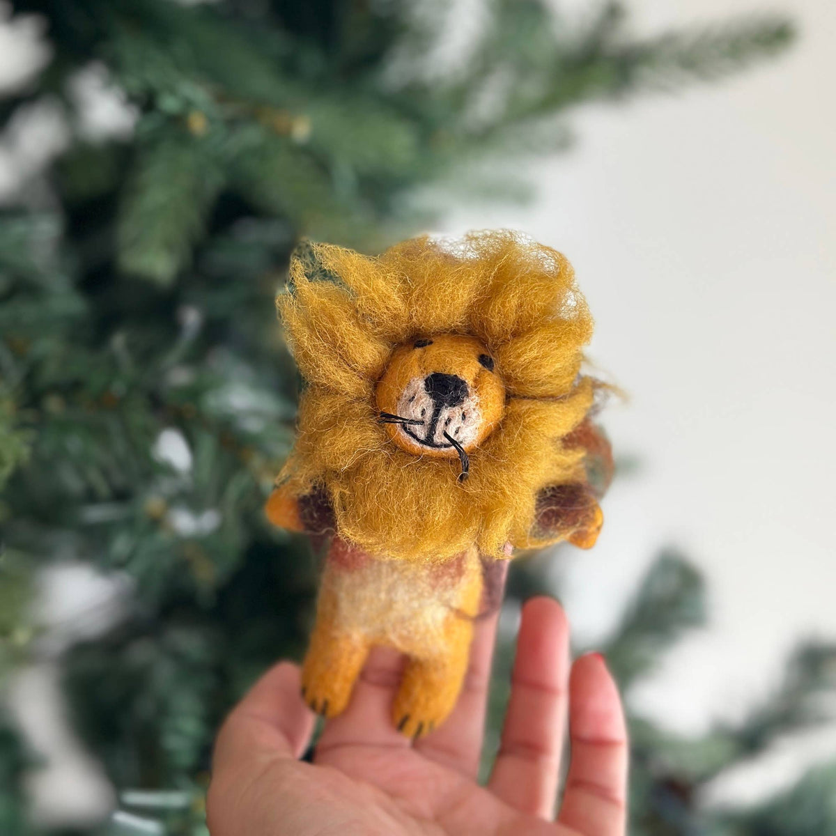 Hand holding a small lion plush toy with a blurred green background