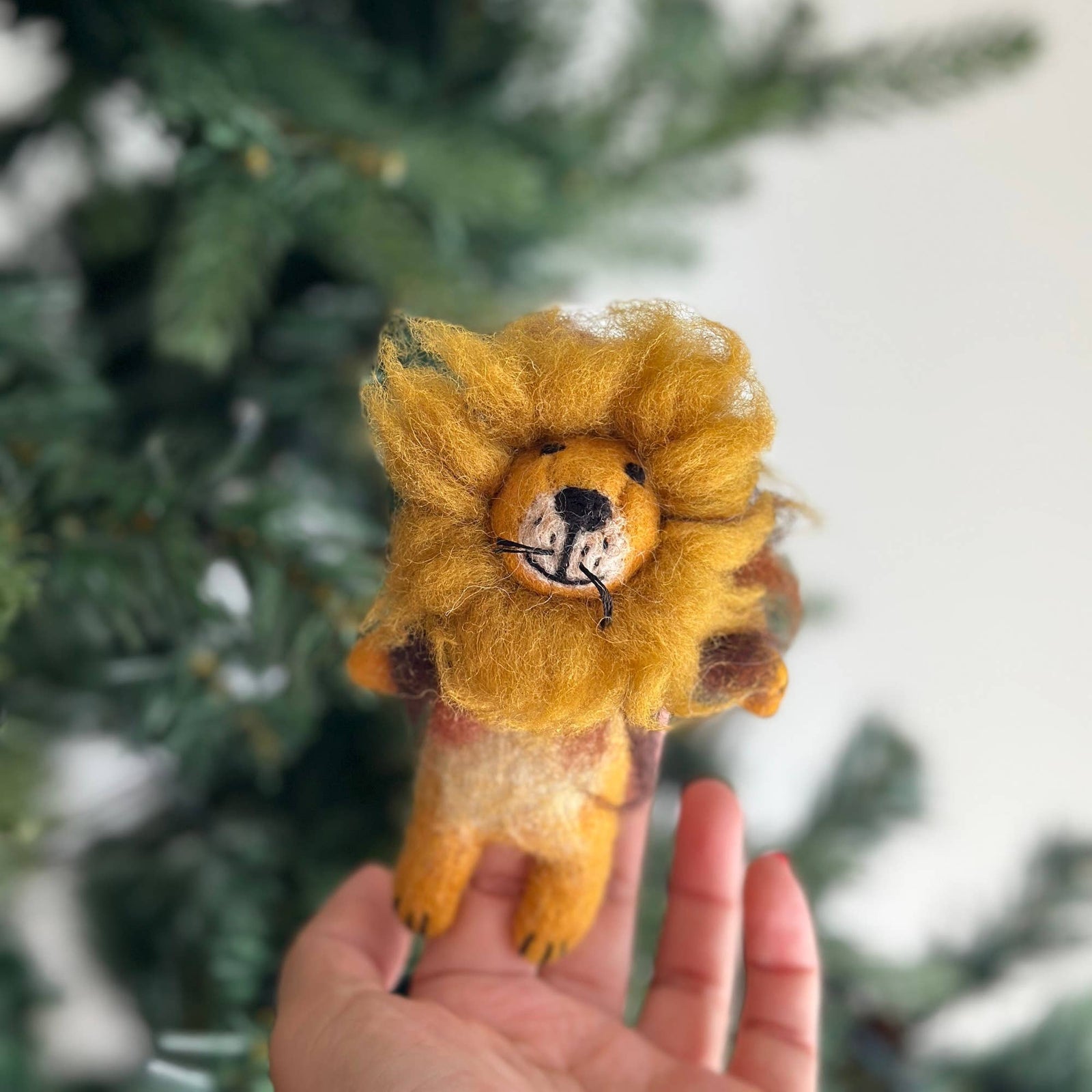 Hand holding a small lion plush toy with a blurred green background