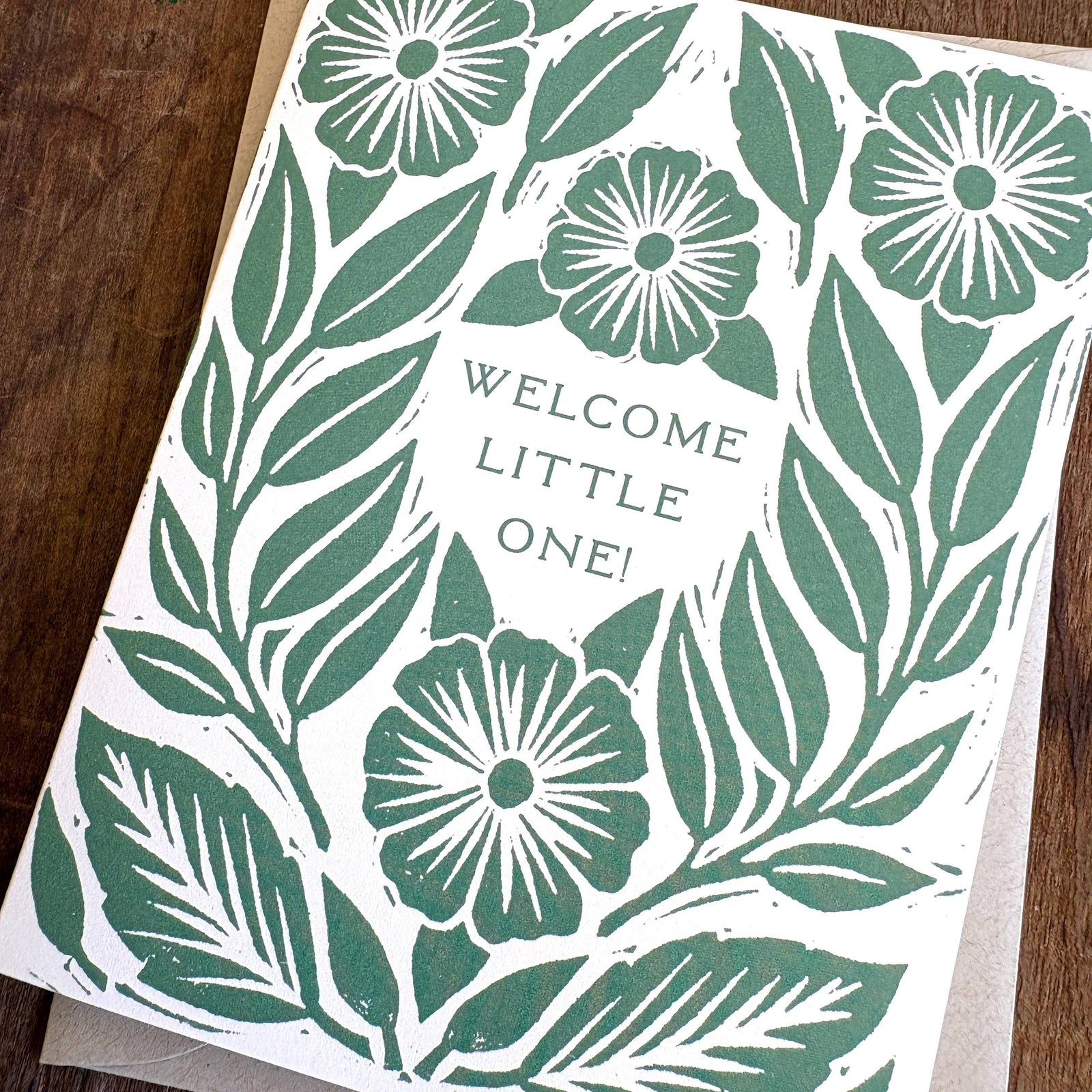 Greeting card with floral design and 'Welcome Little One!' text on a wooden surface