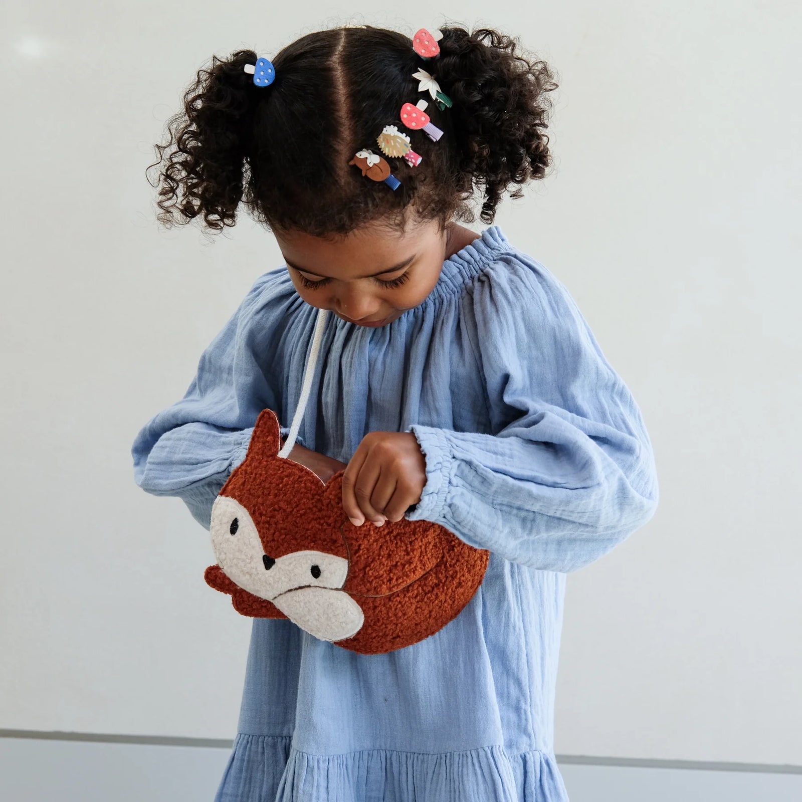Child holding a fox-shaped purse against a plain background