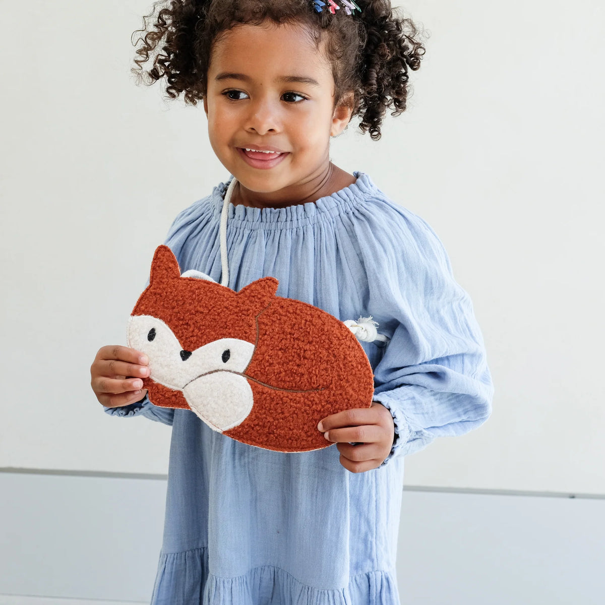 Child holding a fox-shaped plush purse against a white background
