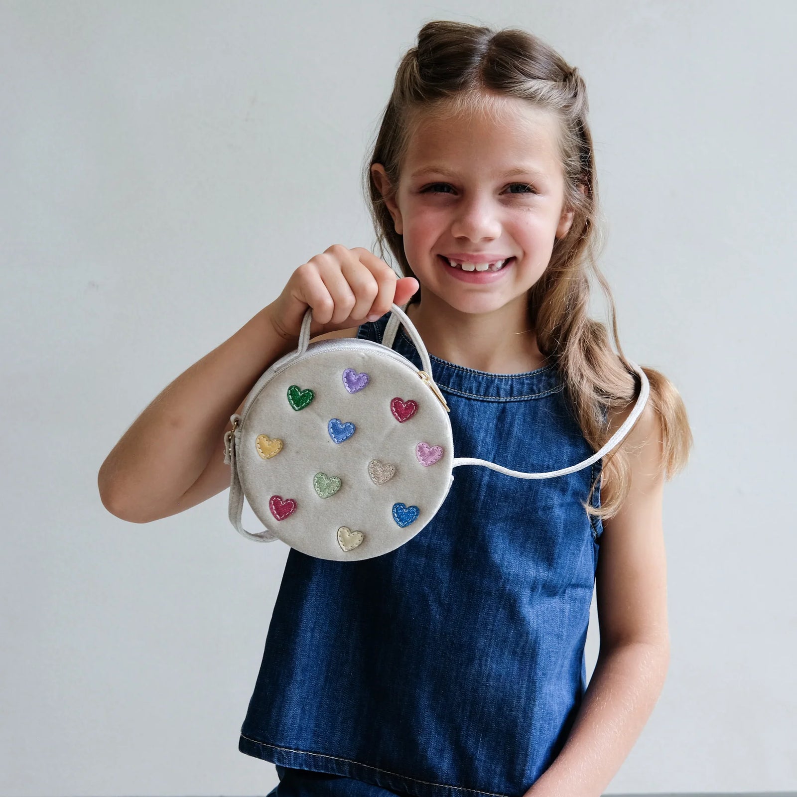 Young girl holding a round bag with heart designs against a plain background