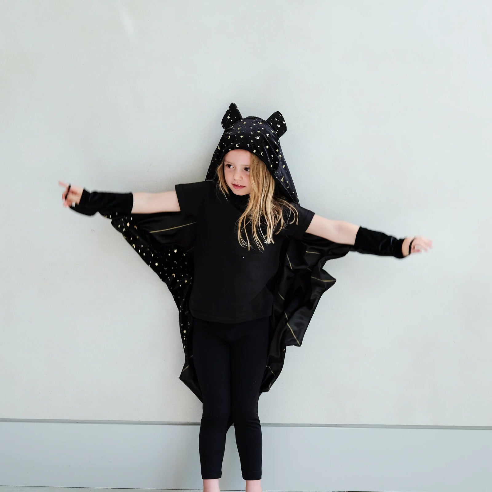 Child wearing a black bat costume with a hood against a light gray background
