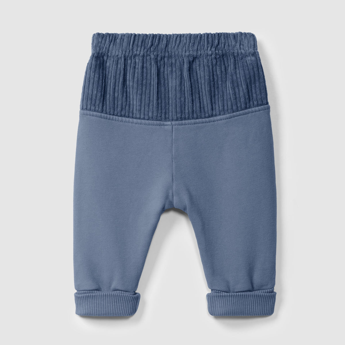 A pair of baby pants in dusty blue, featuring a darker blue ribbed elastic waistband and matching ribbed ankle cuffs, shown against a light gray background.