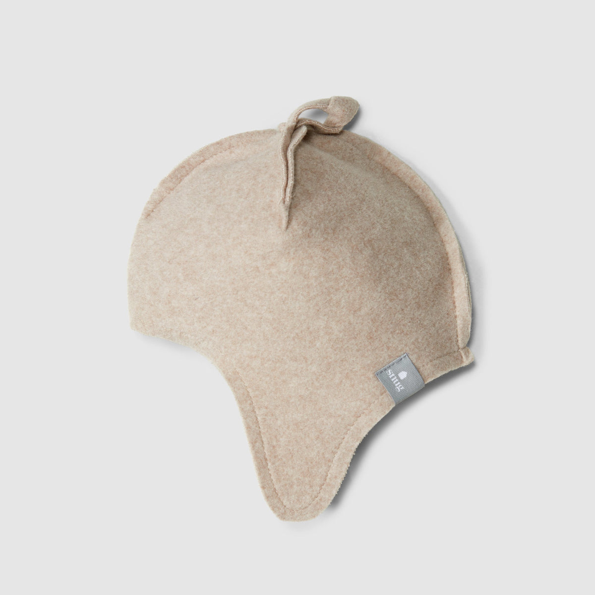 A light beige knit baby beanie hat with ear flaps and a small gray brand tag, shown on a neutral light gray background.