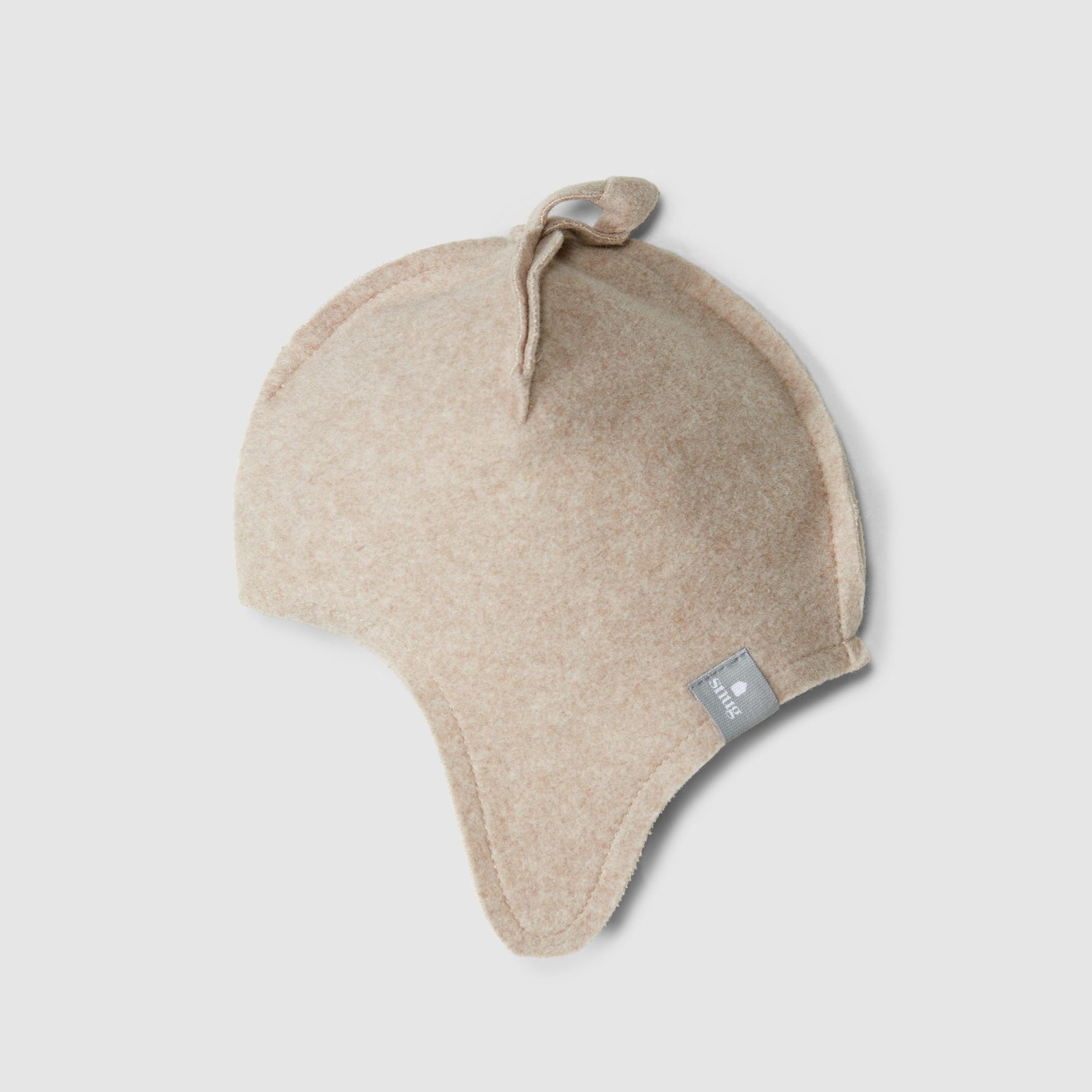 A light beige knit baby beanie hat with ear flaps and a small gray brand tag, shown on a neutral light gray background.