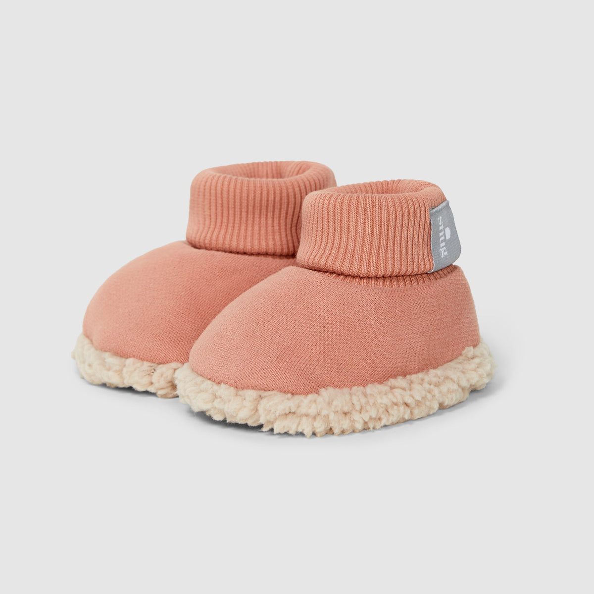 A pair of baby booties in a dusty rose pink knit fabric with a cream sherpa fleece trim and sole, shown on a light gray background.