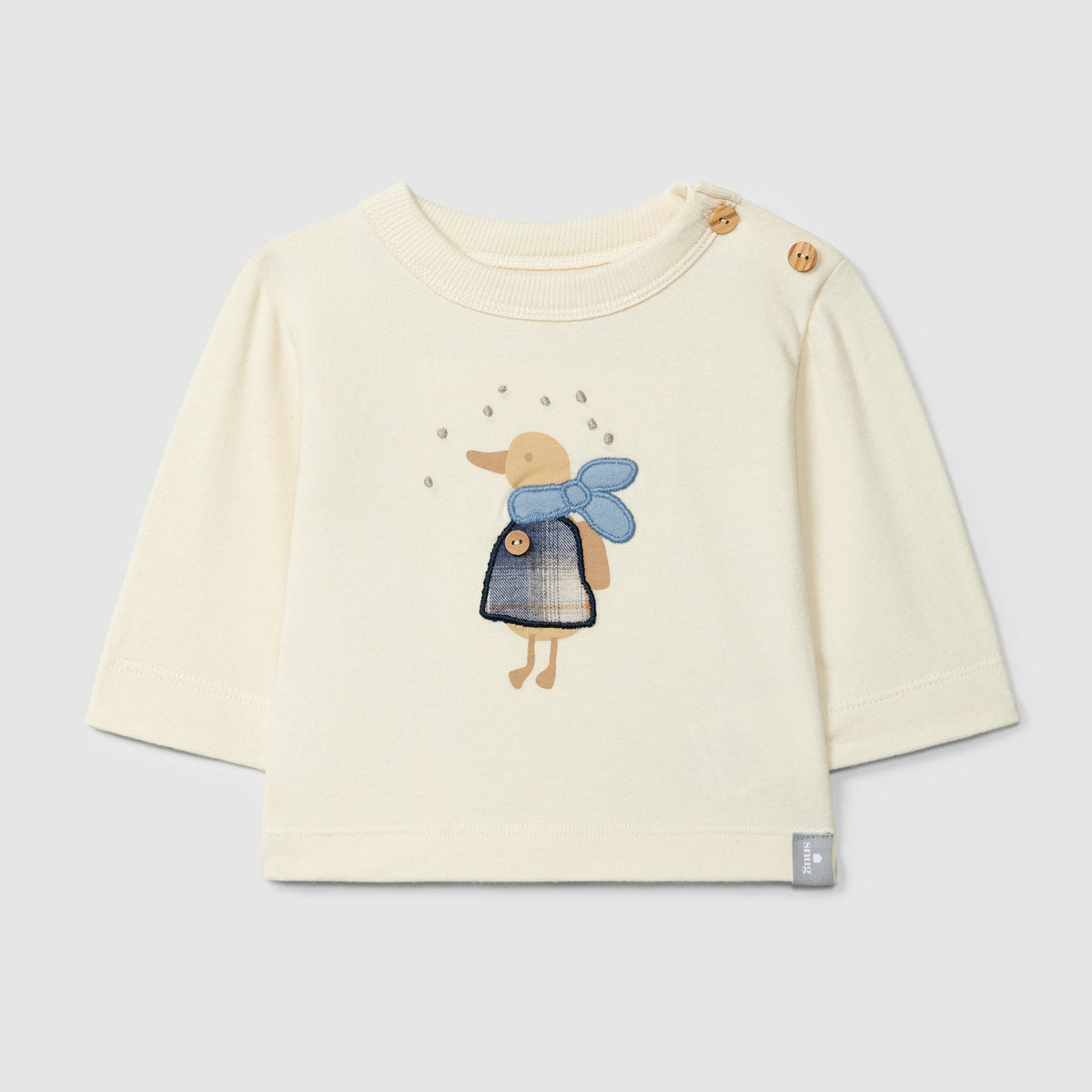 A cream-colored long-sleeve baby top featuring a central graphic of a duckling wearing a blue dress and scarf, with decorative buttons on the shoulder and a small brand tag near the hem.