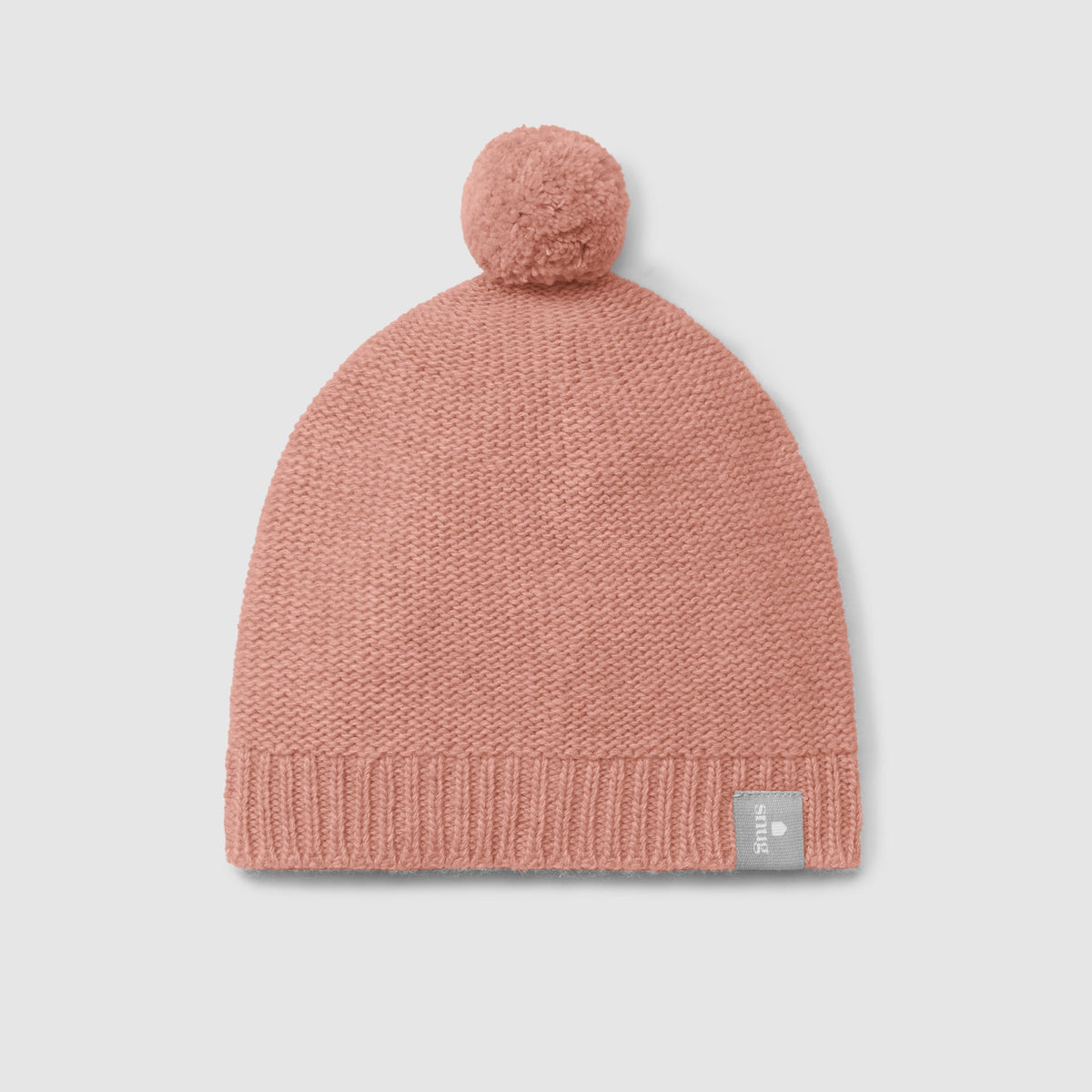 A dusty pink knit beanie with a matching pom-pom on top and a small gray brand tag on the lower right edge, shown against a light gray background.