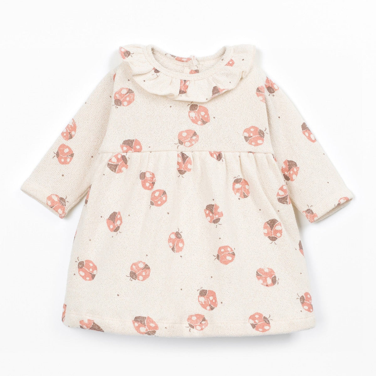 A long-sleeve baby dress in cream with a scattered print of pinkish-red ladybugs and small dark dots, featuring a ruffled collar, shown on a plain white background.