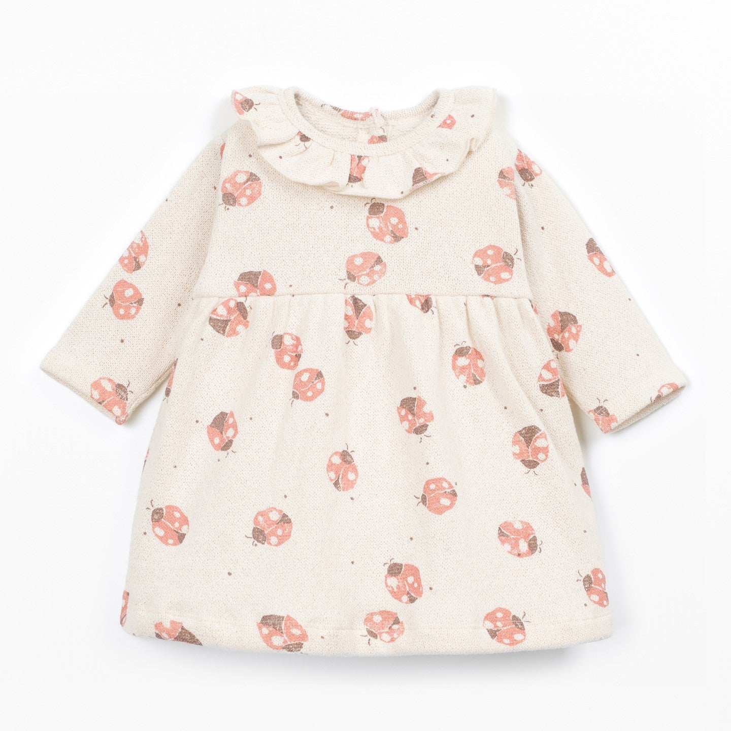 A long-sleeve baby dress in cream with a scattered print of pinkish-red ladybugs and small dark dots, featuring a ruffled collar, shown on a plain white background.
