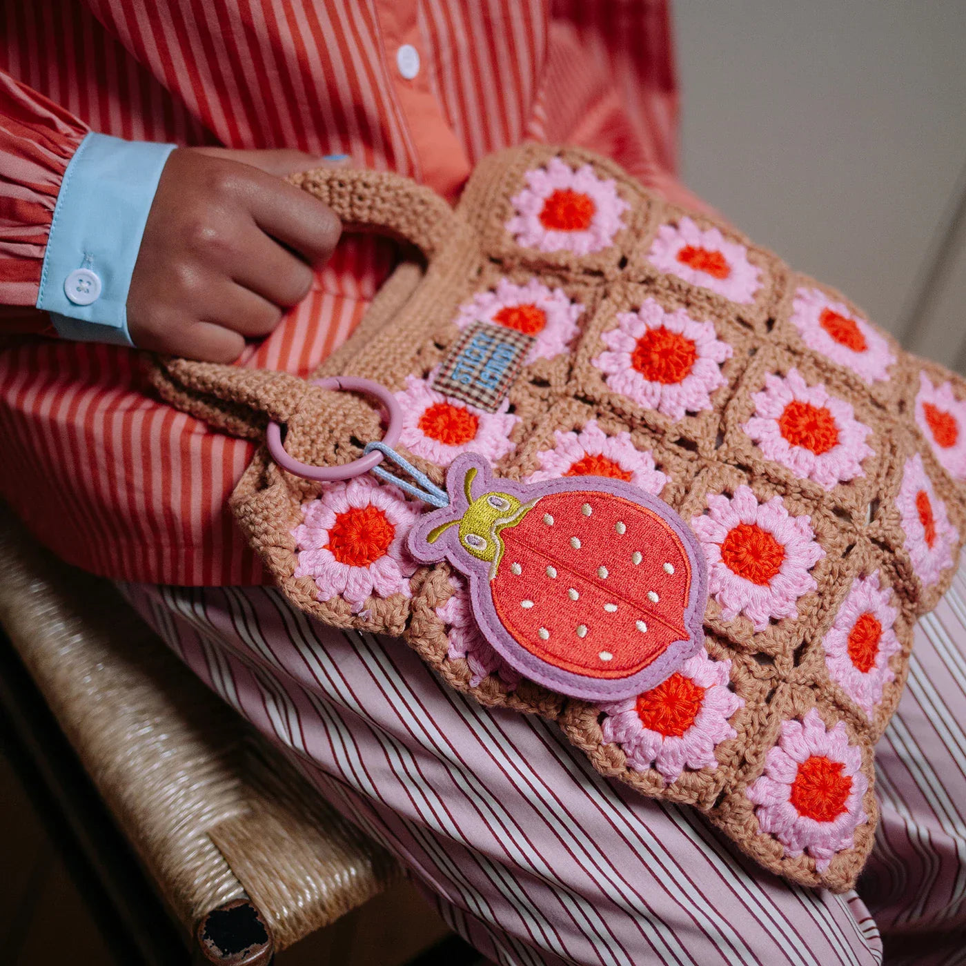 Child wearing a red striped outfit with a blue floral-patterned bag against a brown background