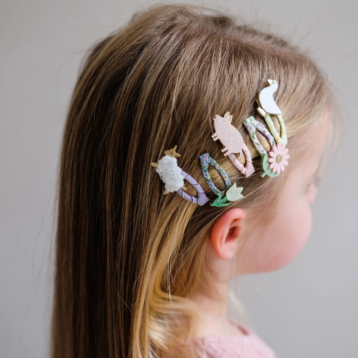 Child with colorful hair clips in their hair against a neutral background