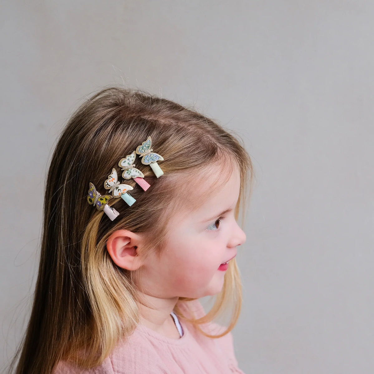Young girl wearing a decorative hair clip with butterflies on a plain background