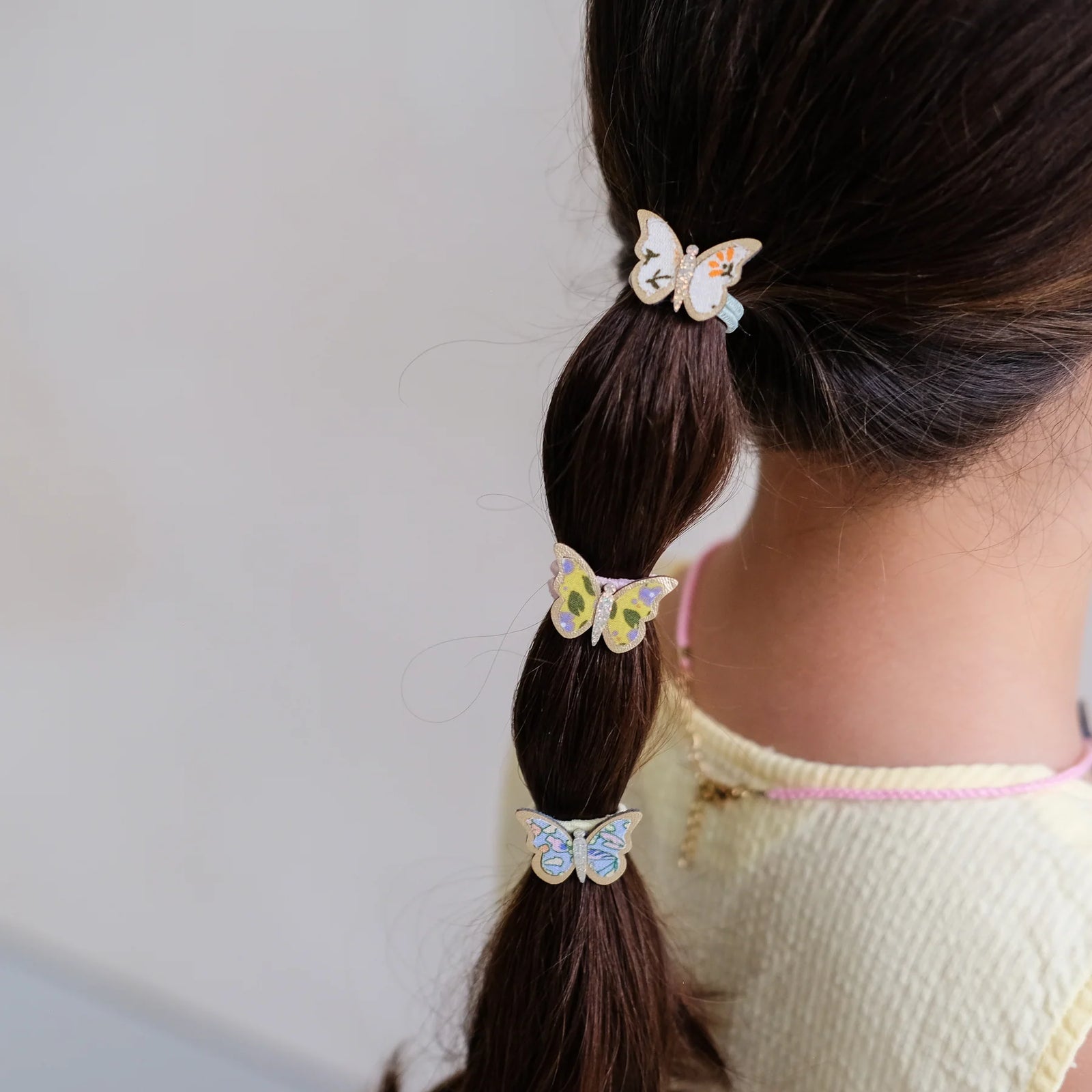 Long blonde hair styled with braids and butterfly hair accessories on a beige background