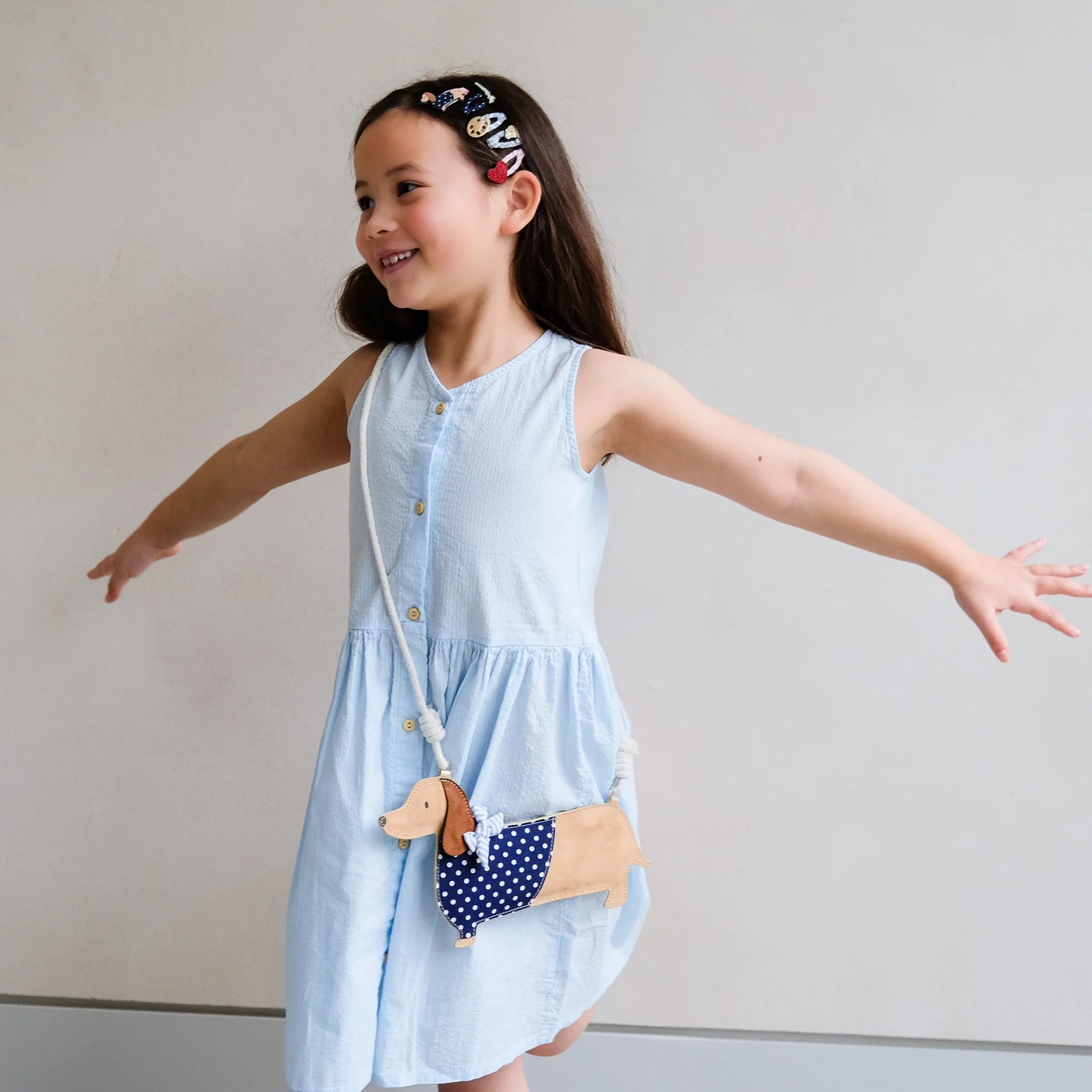 Young girl in a striped outfit holding a plush dog bag against a beige background