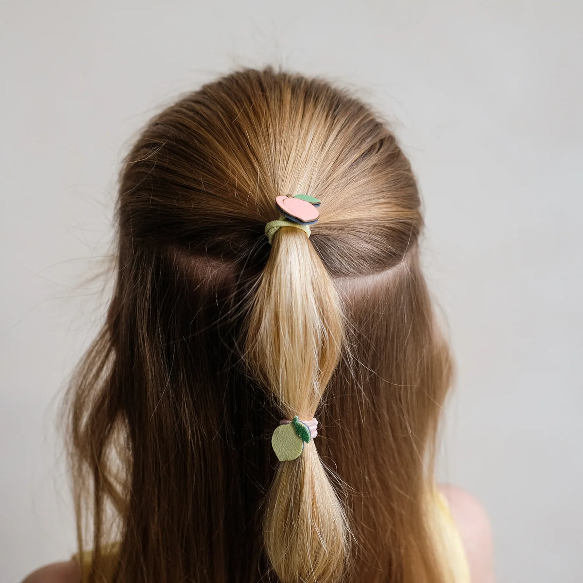 Person with a ponytail using a decorative hair tie against a plain background
