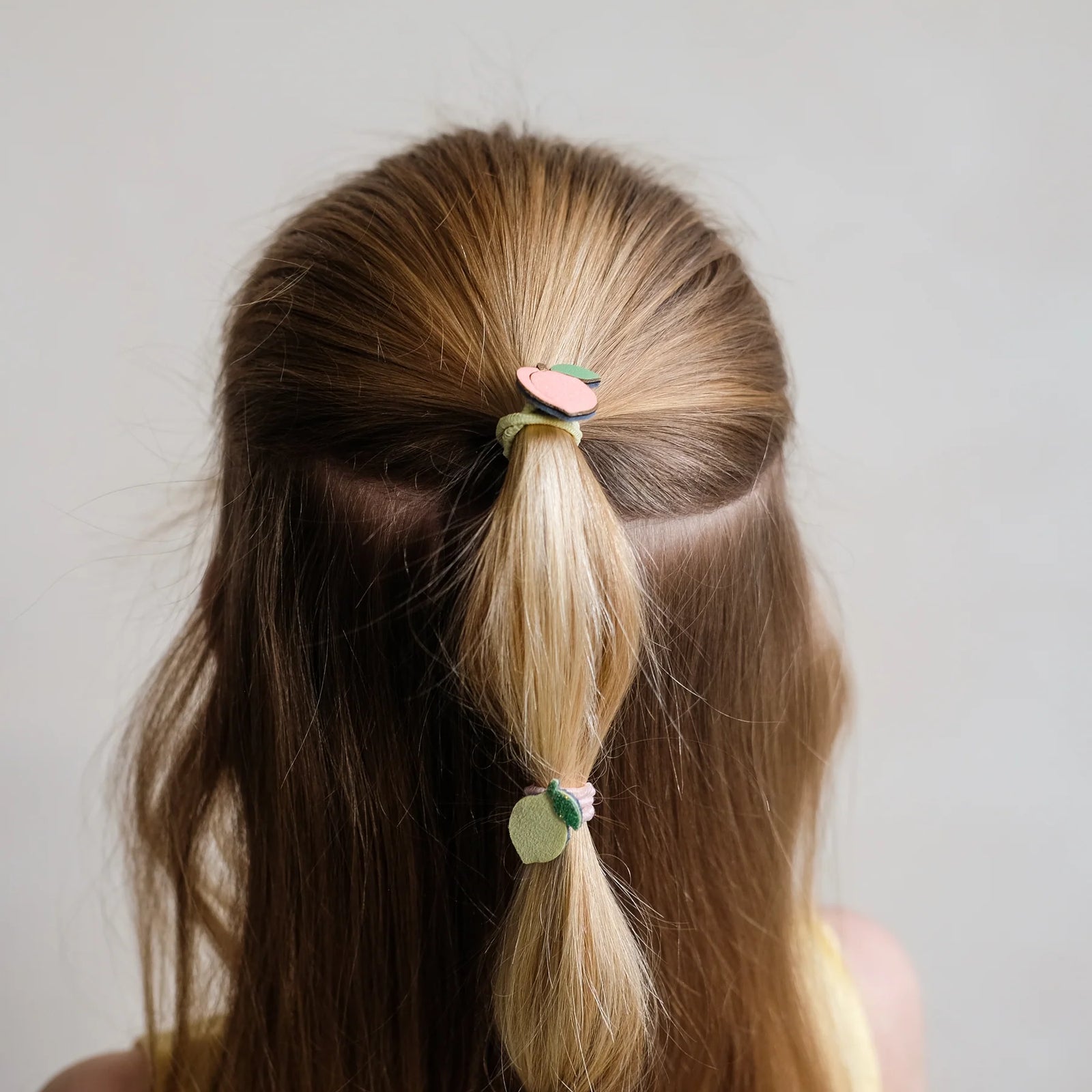 Person with a ponytail using a decorative hair tie against a plain background