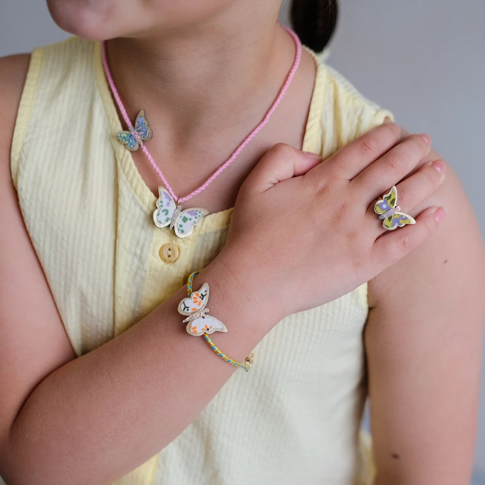 Child wearing a butterfly-themed necklace, bracelet, and ring on a plain background